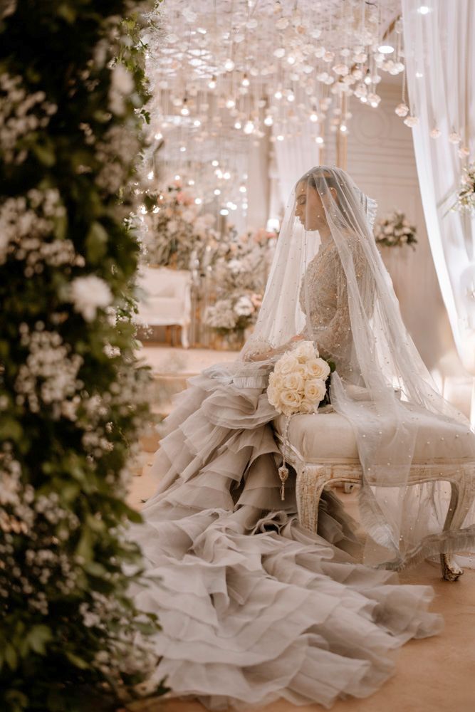Bride seated in profile on a tufted bench, white rose bouquet in her lap, Sheraz & Nawal's wedding at Nishat Hotel, Lahore
