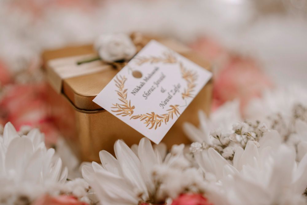 Close-up of the gold nikah favor box and tag nestled among white and pink flowers, Sheraz & Nawal's wedding at Nishat Hotel, Lahore