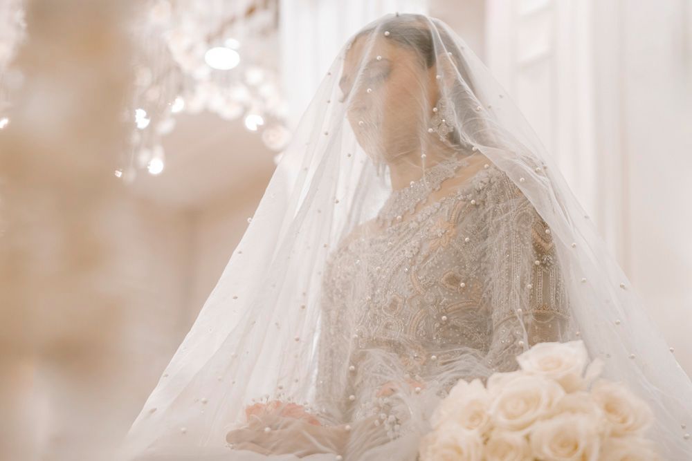 Bride beneath her veil holding a white rose bouquet, soft golden light around her, Sheraz & Nawal's wedding at Nishat Hotel, Lahore