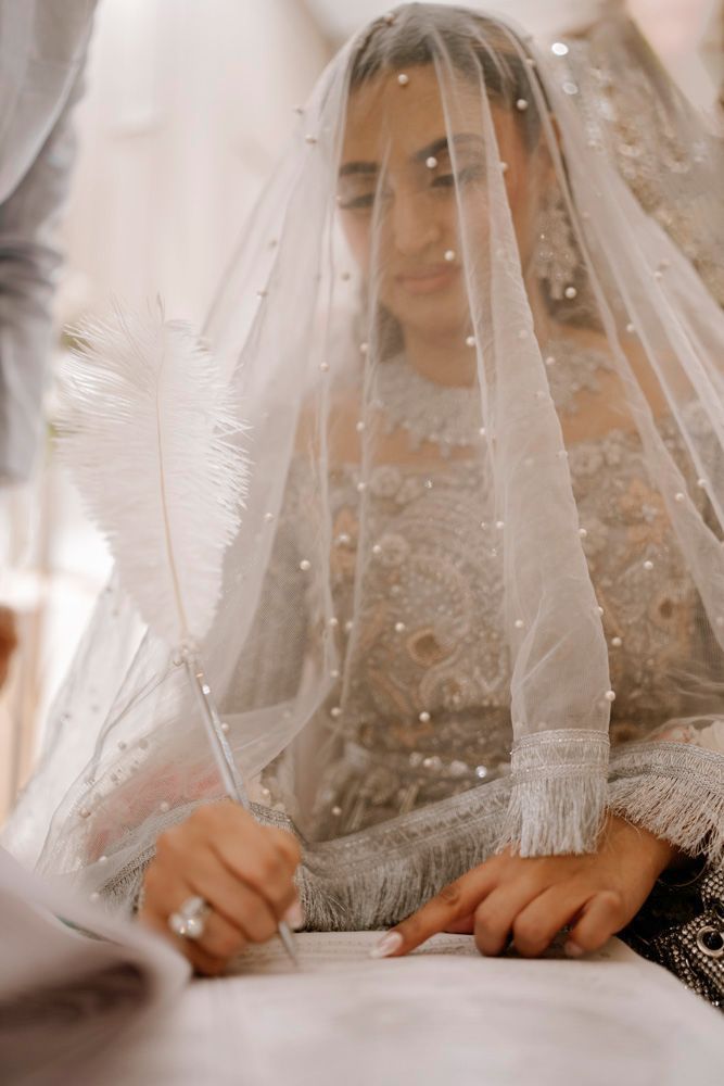Bride signing the nikah register with a white feather quill, smiling beneath her veil, Sheraz & Nawal's wedding at Nishat Hotel, Lahore