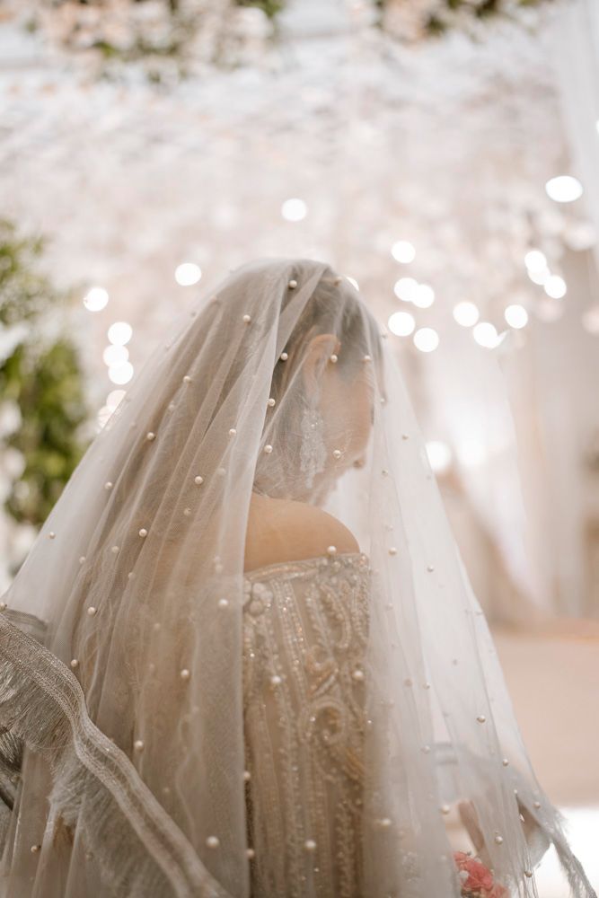 Bride viewed from behind beneath her veil, soft chandelier bokeh in the background, Sheraz & Nawal's wedding at Nishat Hotel, Lahore