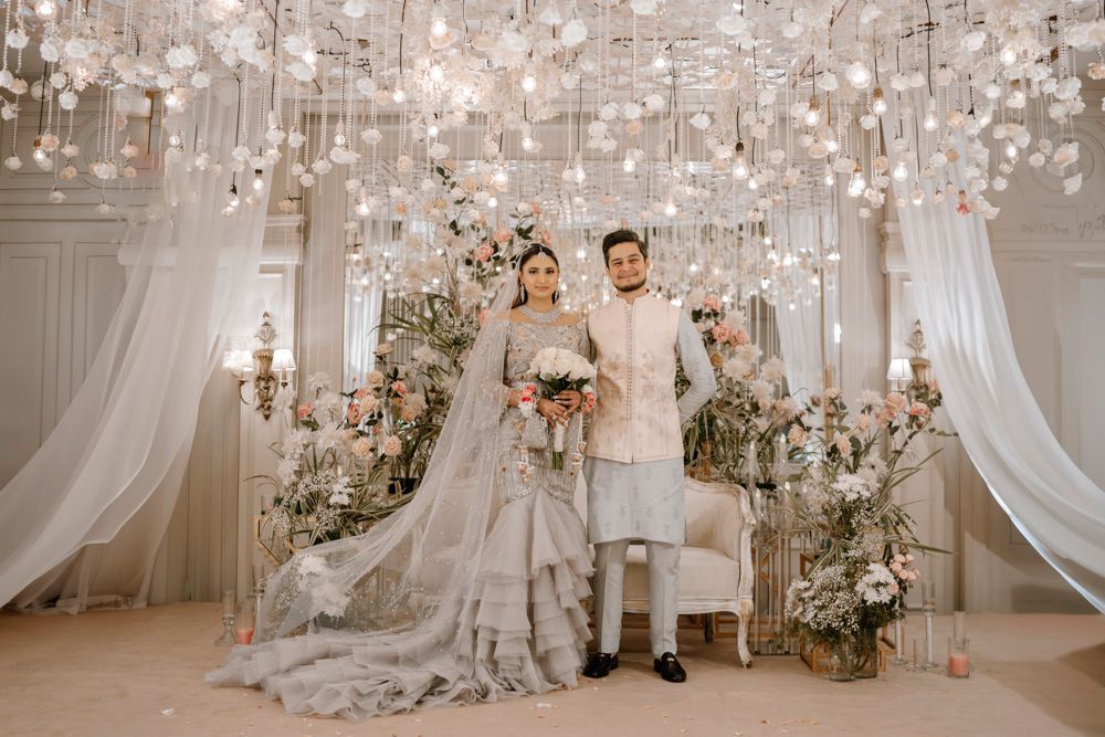Bride and groom standing together in the reception hall beneath hanging floral lights, Sheraz & Nawal's wedding at Nishat Hotel, Lahore