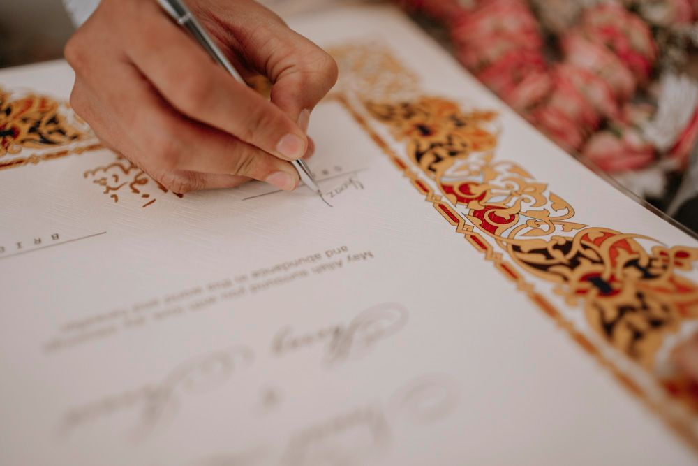 Detail of a hand signing the gold-bordered nikah certificate with a fountain pen, Sheraz & Nawal's wedding at Nishat Hotel, Lahore