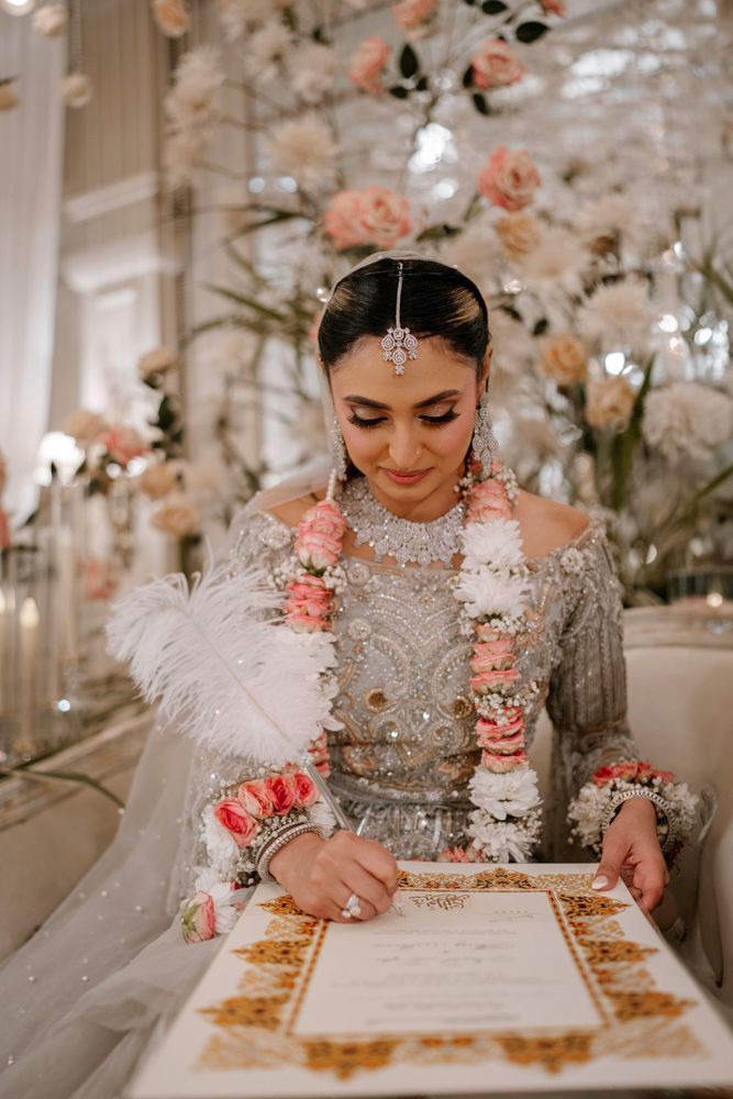 Bride signing the nikah certificate with a feather quill, wearing a pink and white flower garland, Sheraz & Nawal's wedding at Nishat Hotel, Lahore