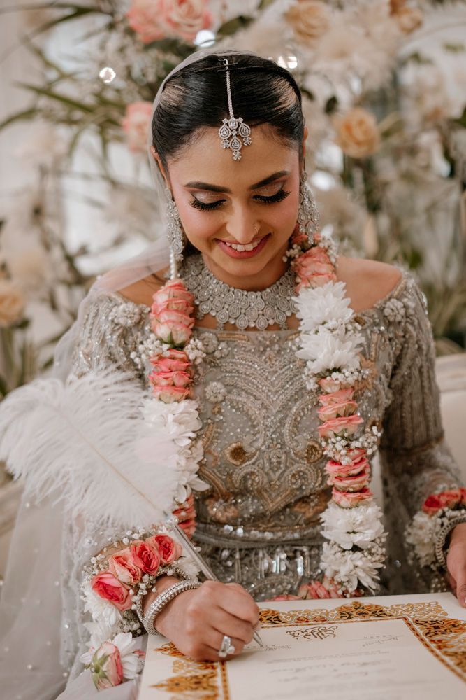 Close-up of the bride smiling while signing the nikah certificate, wearing her flower garland, Sheraz & Nawal's wedding at Nishat Hotel, Lahore