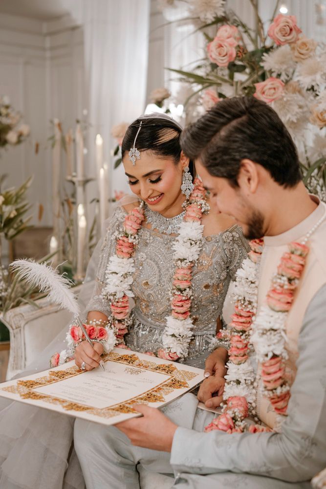 Bride and groom seated together signing the nikah certificate, both wearing flower garlands, Sheraz & Nawal's wedding at Nishat Hotel, Lahore