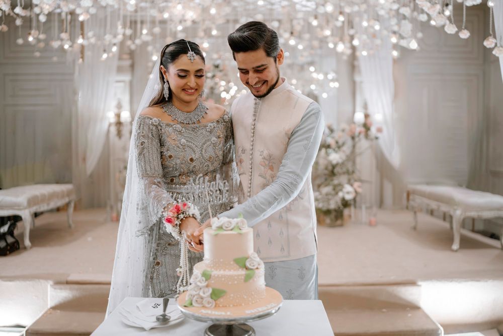 Bride and groom cutting their wedding cake together beneath hanging floral chandeliers, Sheraz & Nawal's wedding at Nishat Hotel, Lahore