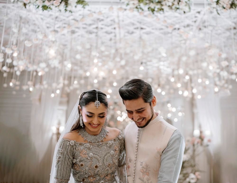 Bride and groom smiling together beneath a canopy of hanging lights and white roses, Sheraz & Nawal's wedding at Nishat Hotel, Lahore