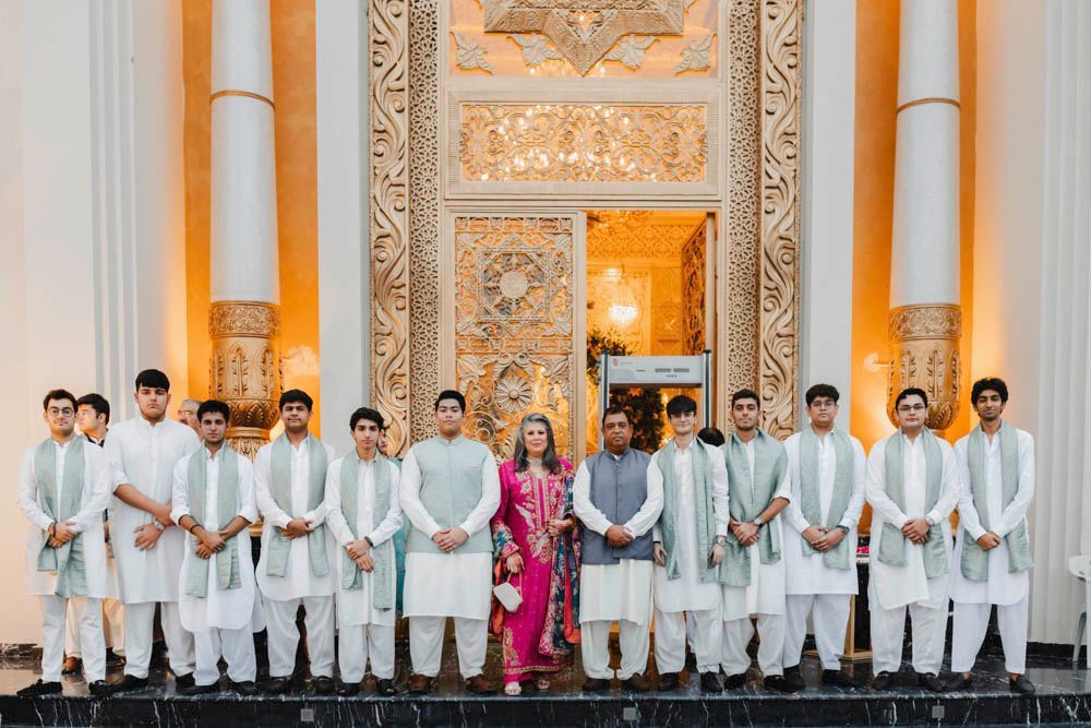 Groomsmen in white kurtas with sage green shawls lining the venue entrance with the groom's parents, Zara & Shuaib's wedding at Garrison Halls, Lahore