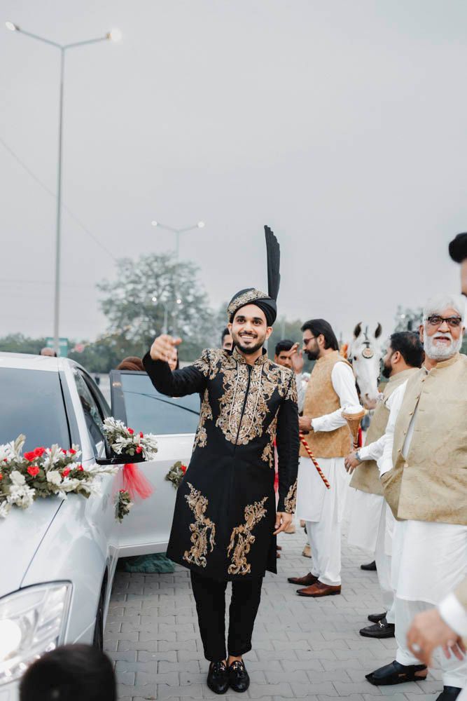 Groom celebrating outdoors beside a flower-decorated car with a white horse nearby during the baraat, Zara & Shuaib's wedding, Lahore