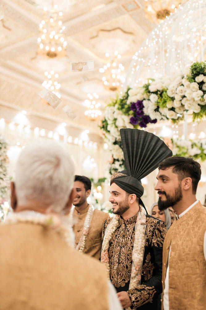 Groom arriving indoors beneath chandeliers as money is showered over him in celebration, Zara & Shuaib's wedding at Garrison Halls, Lahore