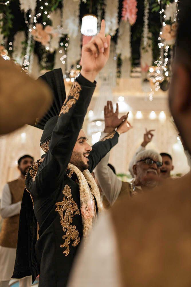 Groom dancing with his arm raised beneath a floral and crystal ceiling installation, Zara & Shuaib's wedding at Garrison Halls, Lahore