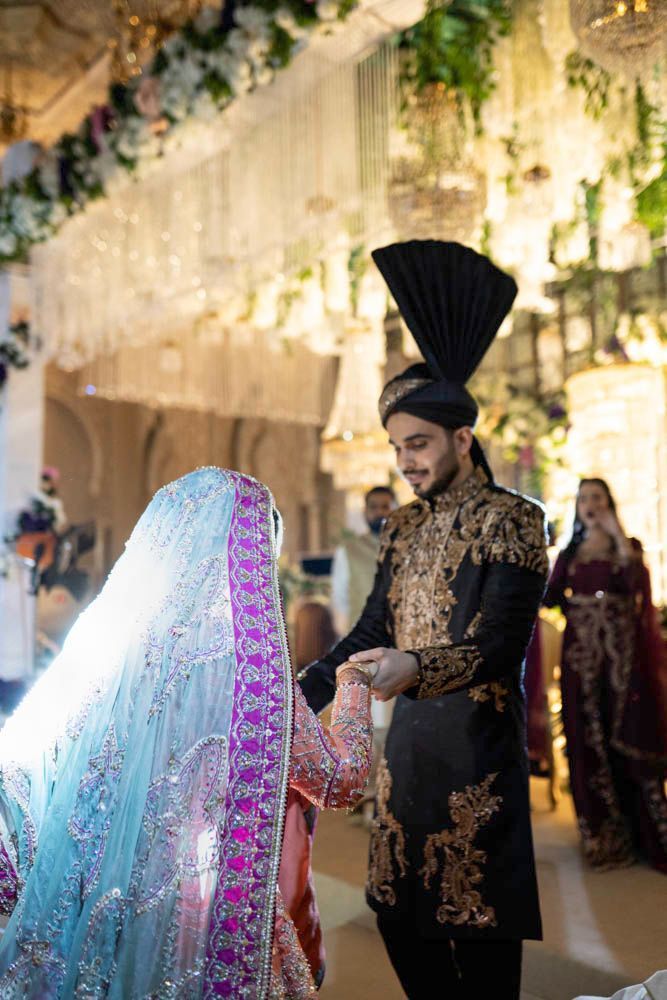 Bride and groom holding hands beneath a floral and crystal archway, Zara & Shuaib's wedding at Garrison Halls, Lahore