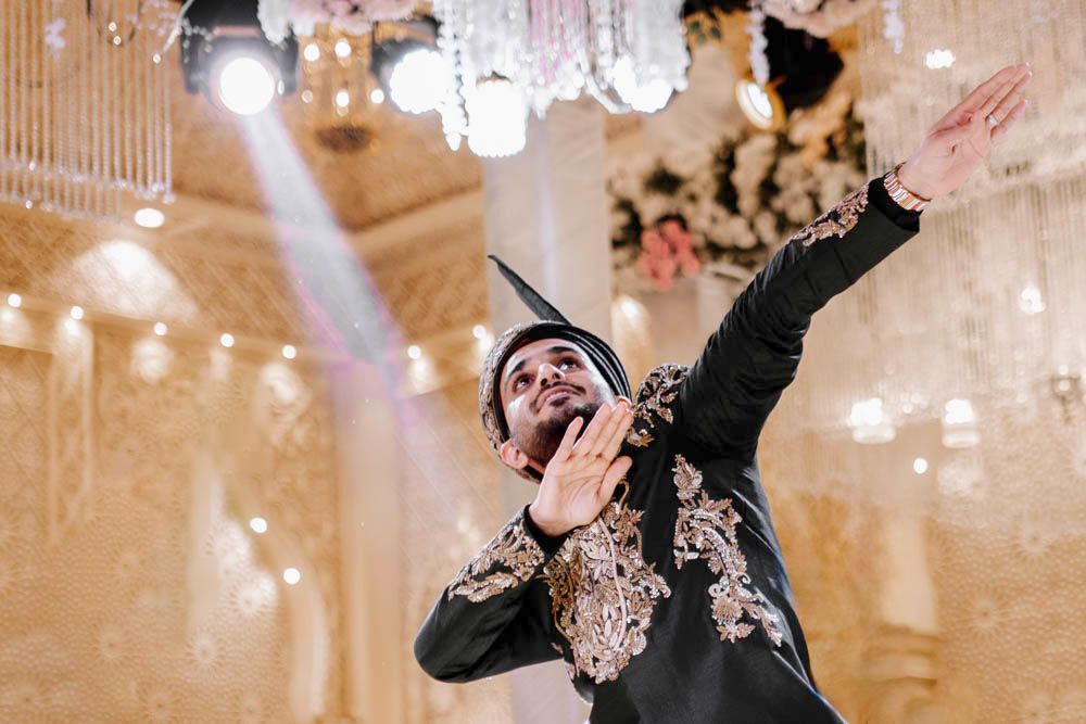 Groom dancing energetically with arms outstretched beneath a spotlight, Zara & Shuaib's wedding at Garrison Halls, Lahore