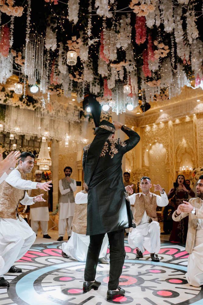 Groom seen from behind dancing on the patterned dance floor as friends cheer, Zara & Shuaib's wedding at Garrison Halls, Lahore