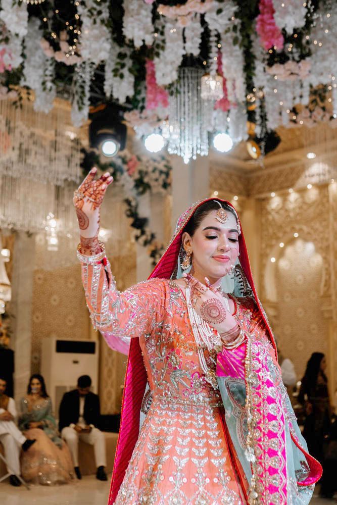 Bride dancing with one hand raised, henna visible on her palm, Zara & Shuaib's wedding at Garrison Halls, Lahore