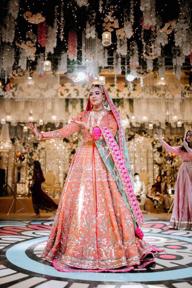Bride dancing with hands raised, guests visible seated behind her, Zara & Shuaib's wedding at Garrison Halls, Lahore