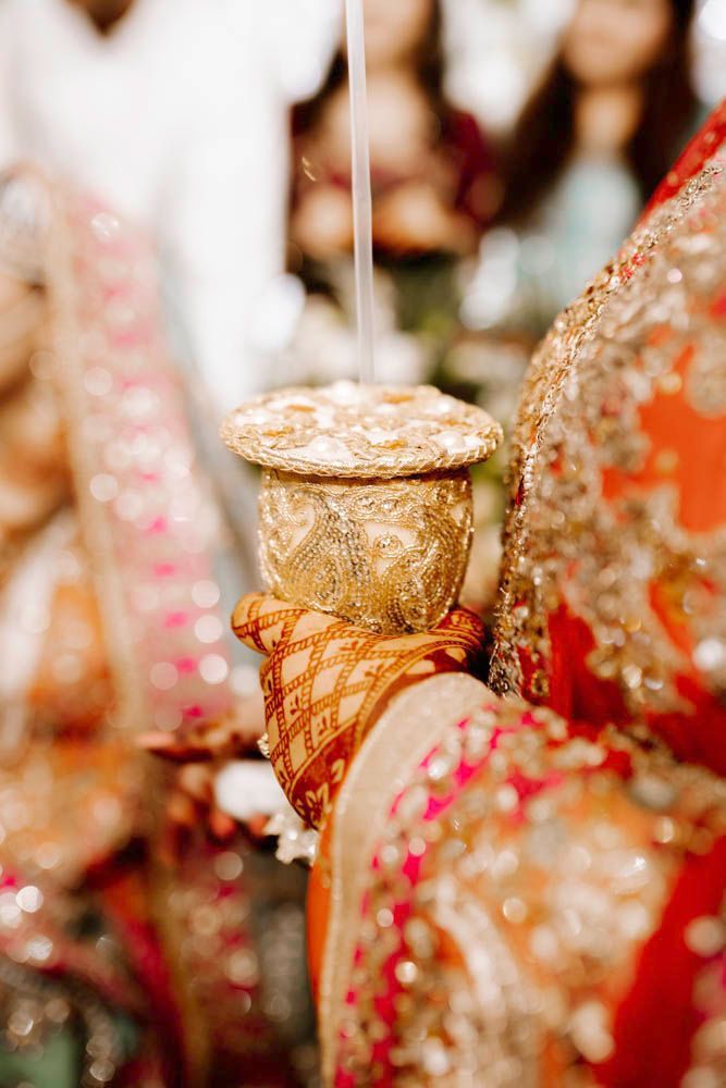 Detail of an embroidered ceremonial cap and henna-painted hand against the bride's red and orange lehenga, Zara & Shuaib's wedding, Lahore