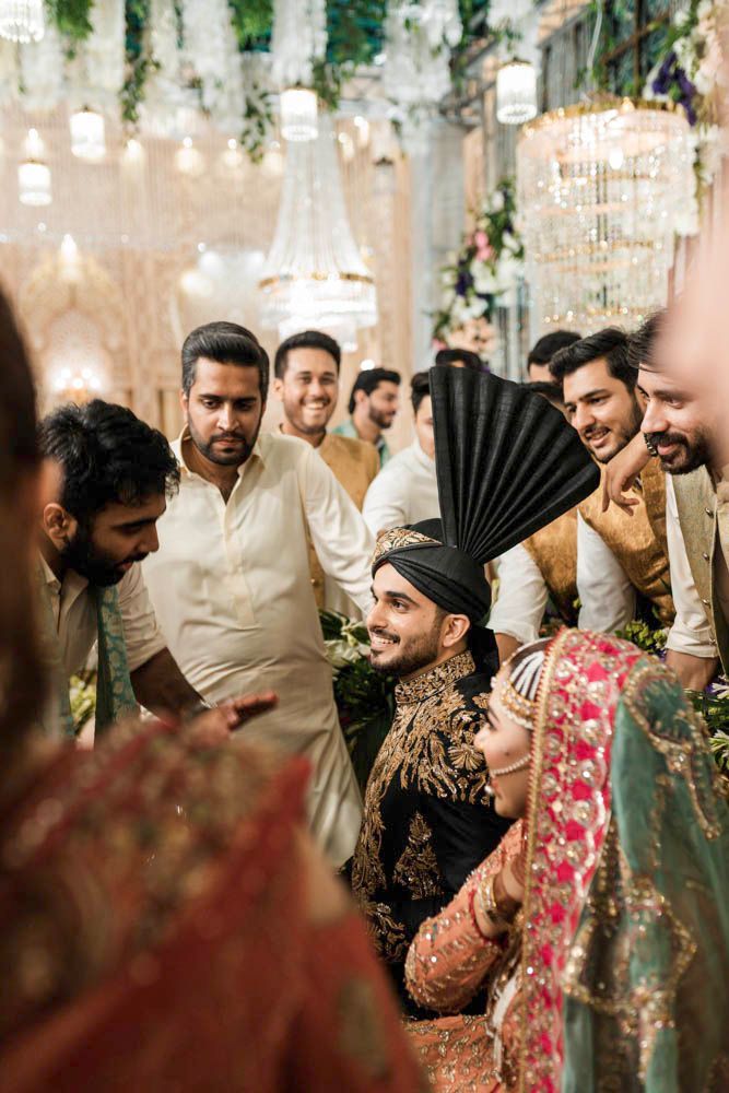 Groom surrounded by laughing friends, bride visible nearby in a green and orange outfit, Zara & Shuaib's wedding, Lahore