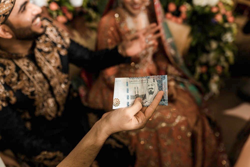 Detail of a foreign banknote being held up in celebration, bride and groom blurred in the background, Zara & Shuaib's wedding, Lahore
