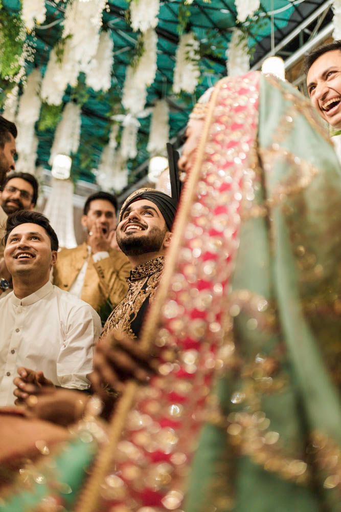 Groom laughing with friends beside the bride in a teal and gold outfit under string lights, Zara & Shuaib's wedding, Lahore