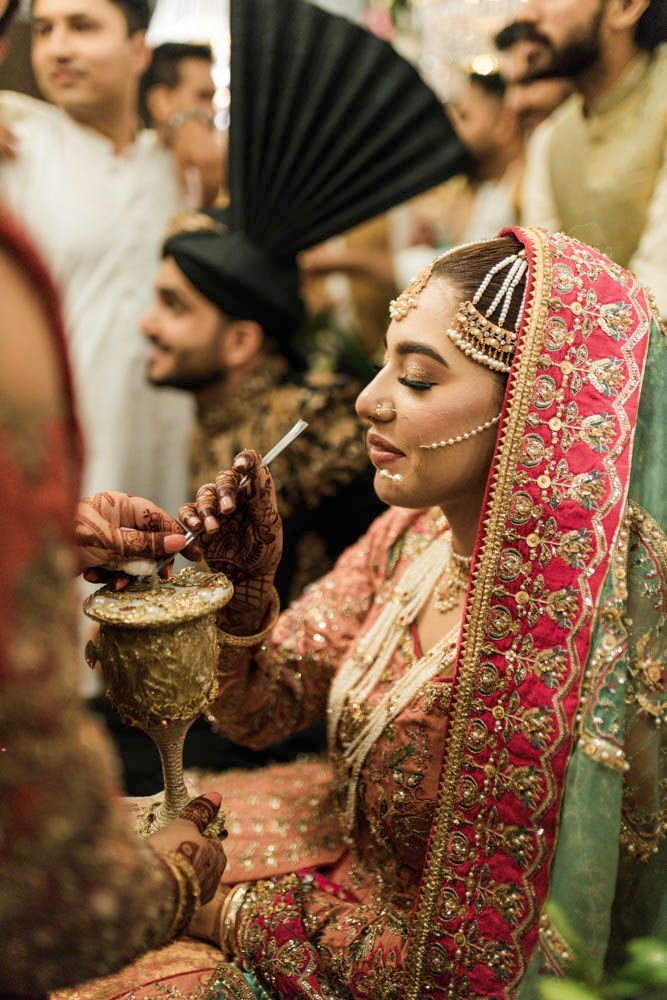 Bride sipping a drink through a straw from an ornate cup, eyes closed, candid moment, Zara & Shuaib's wedding, Lahore