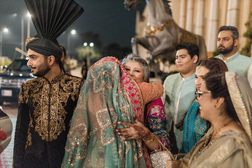 Bride embracing an older family member outside the venue near a sculptural horse statue at night, Zara & Shuaib's wedding, Lahore