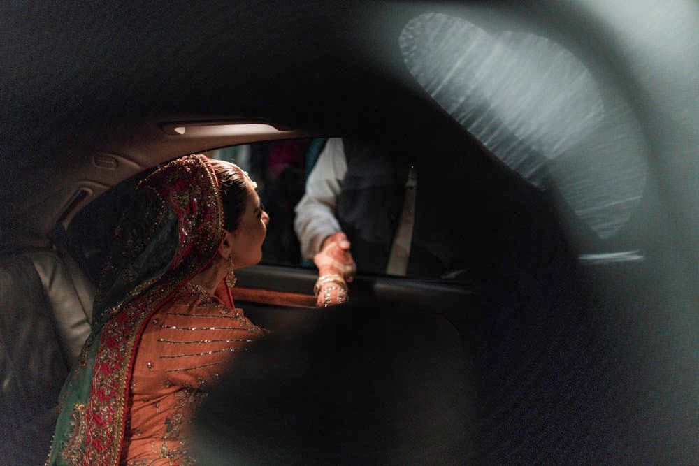 Bride reaching to hold the groom's hand through the car door as she departs at night, Zara & Shuaib's wedding, Lahore
