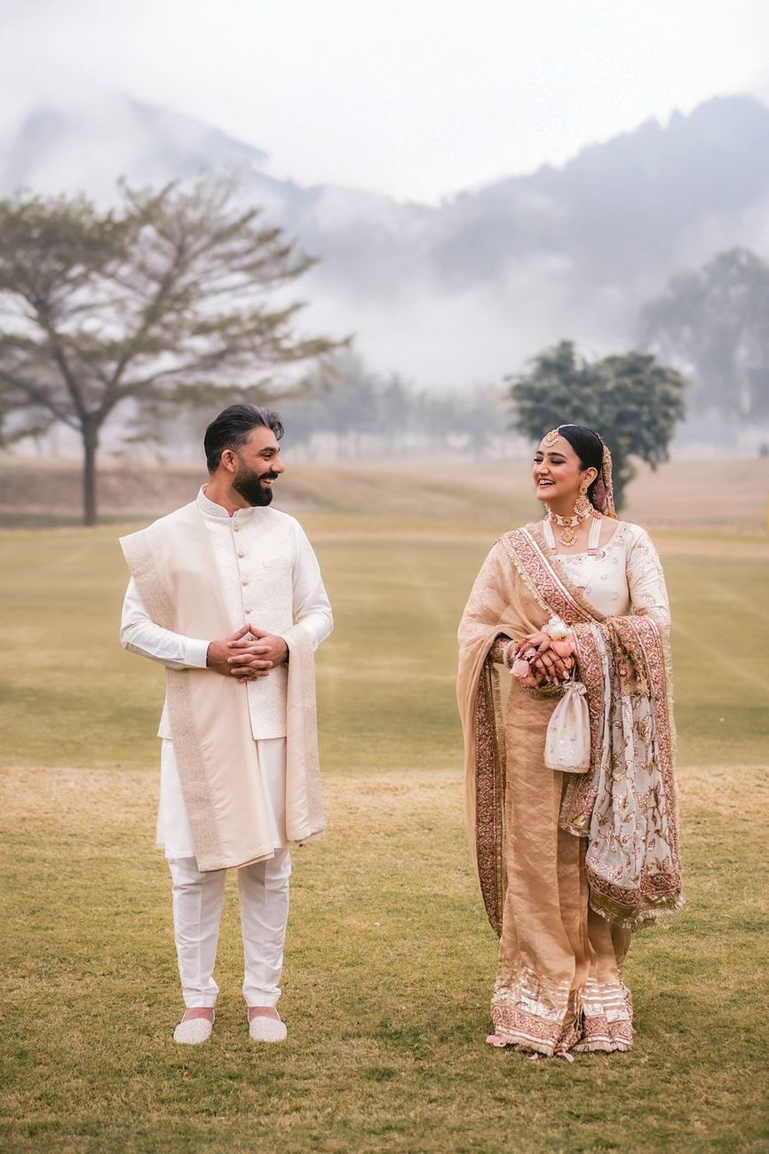 Bride and groom standing apart smiling at each other on a misty open field