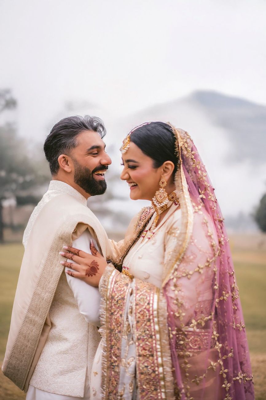 Close portrait of the bride and groom laughing together, misty hills behind them
