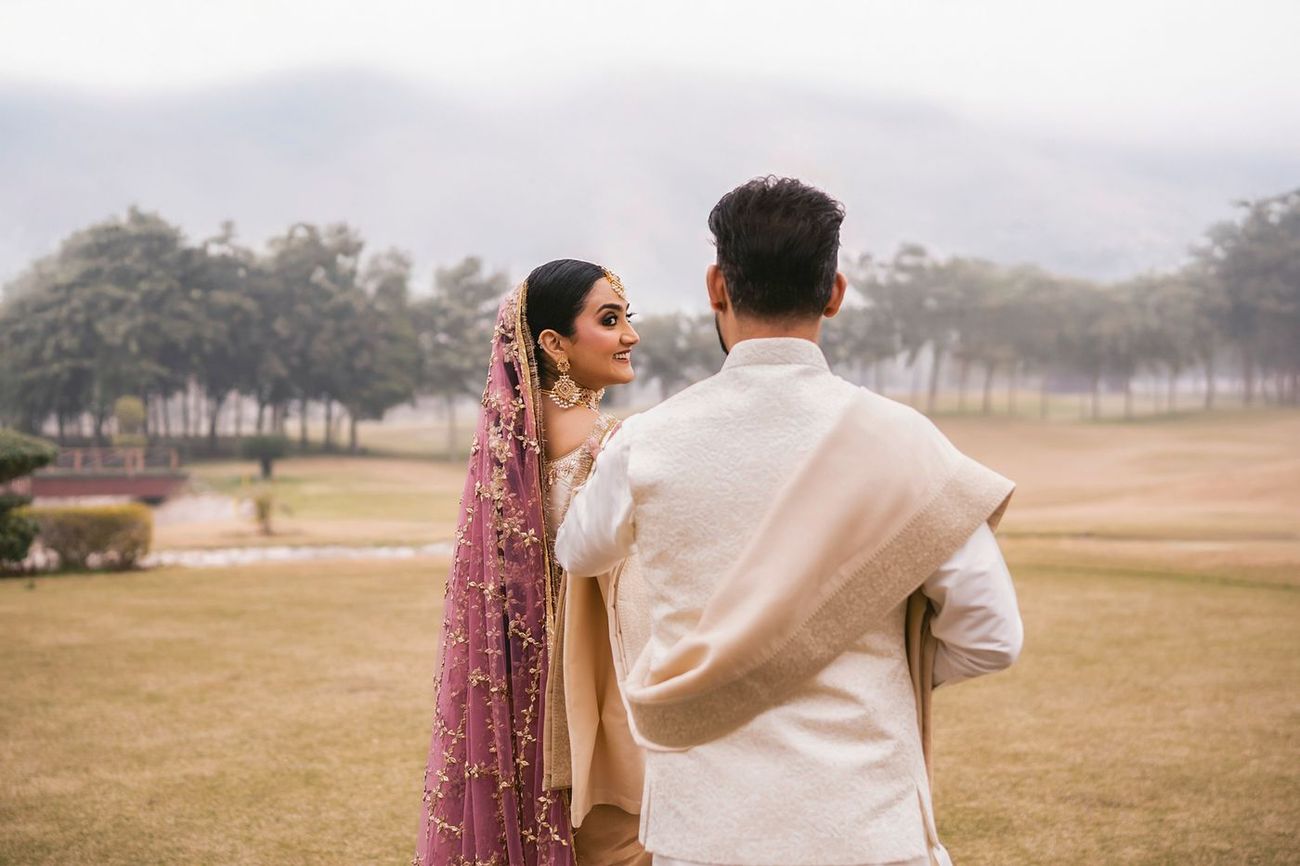 Back view of the couple on the misty field, bride glancing over her shoulder