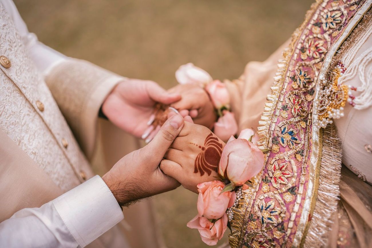 Close detail of the couple's joined hands holding pink roses