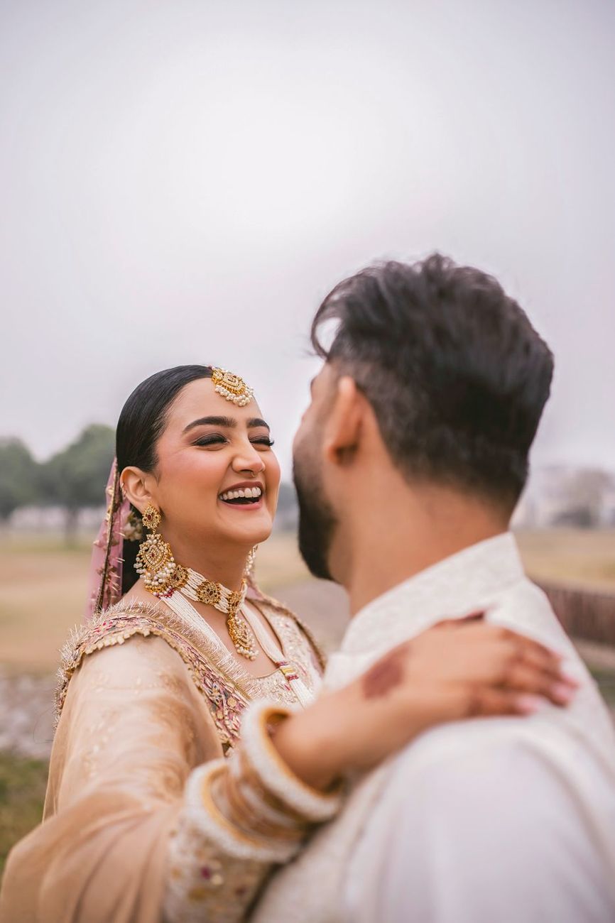 Close-up of the bride laughing with her arm around the groom's shoulder, shot over his shoulder