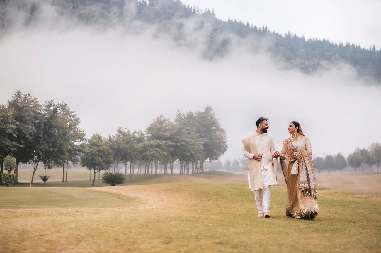 Wide-angle shot of the couple walking on a mist-covered lawn with a tree-lined fairway