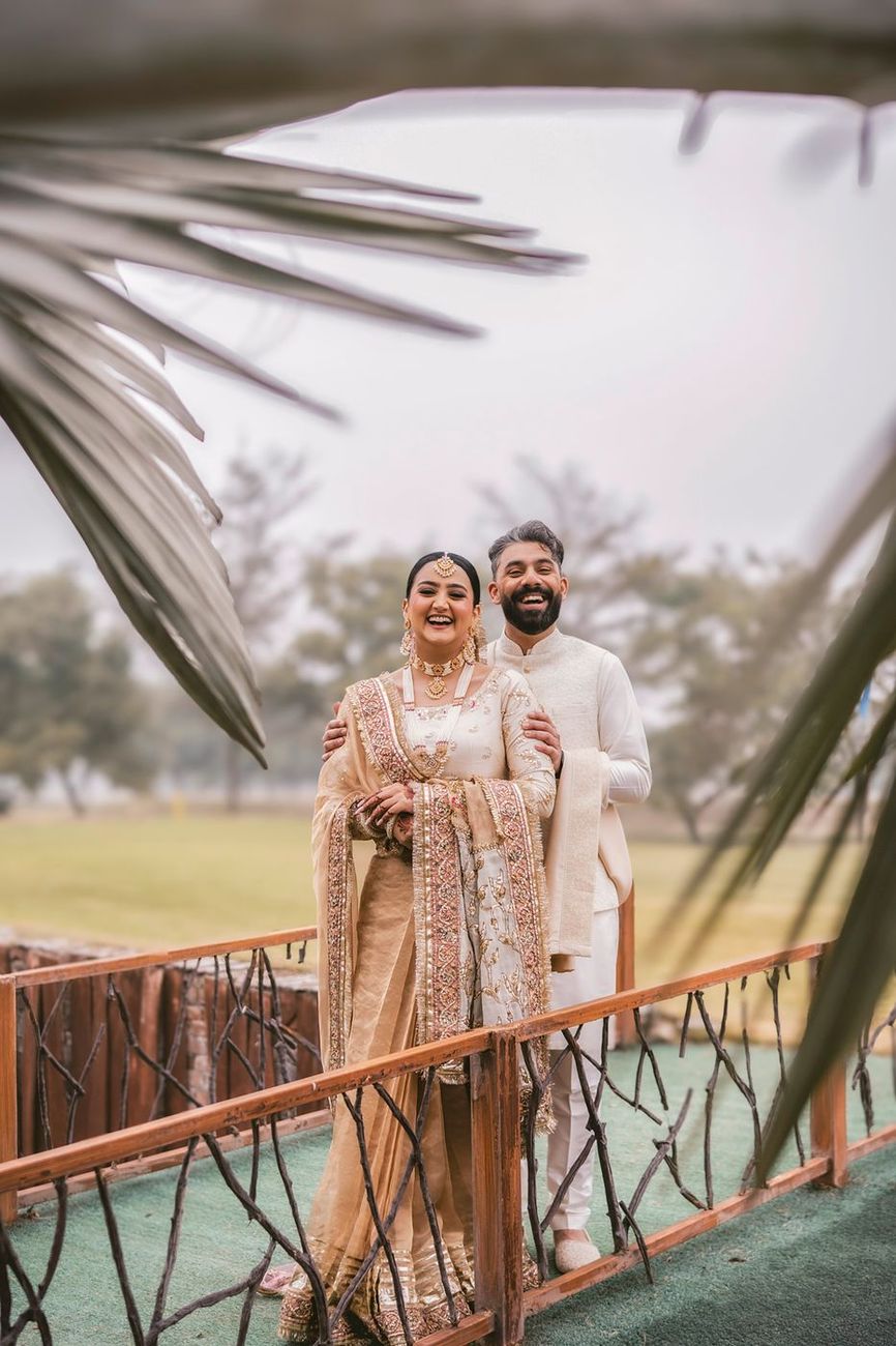 Couple smiling on a small wooden bridge, palm fronds framing the foreground