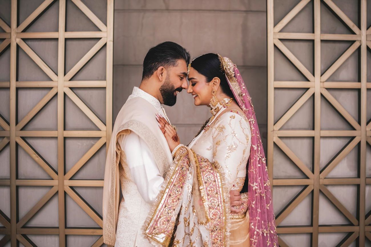 Bride and groom embracing forehead-to-forehead against the same latticed wall