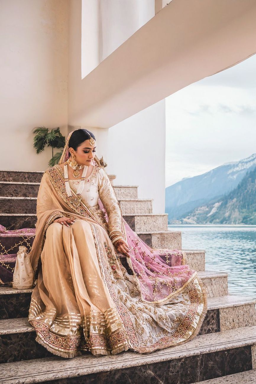 Solo bridal portrait seated on the staircase, gown spread across the steps, lake and mountains beyond