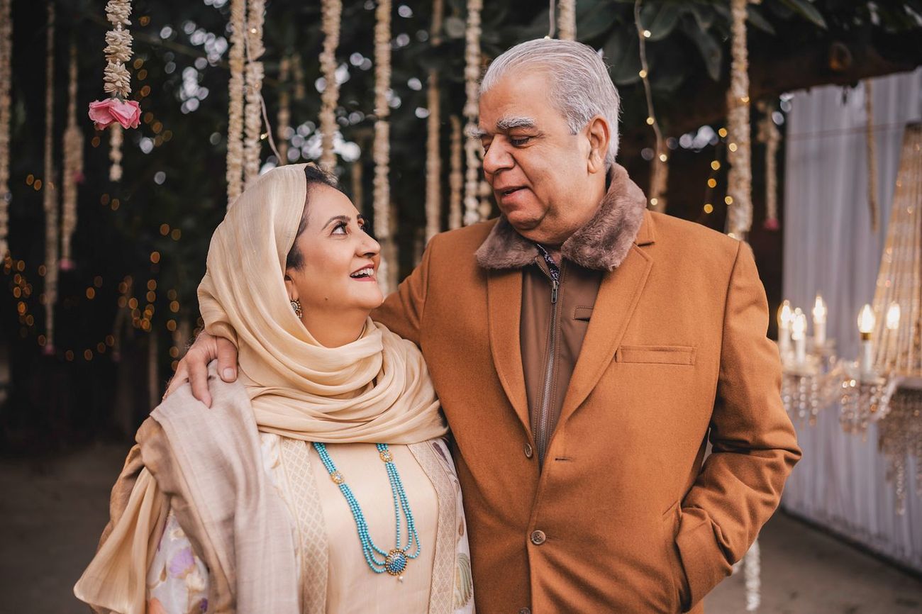 Older couple, likely the bride's parents, posed together at the evening venue under hanging floral garlands