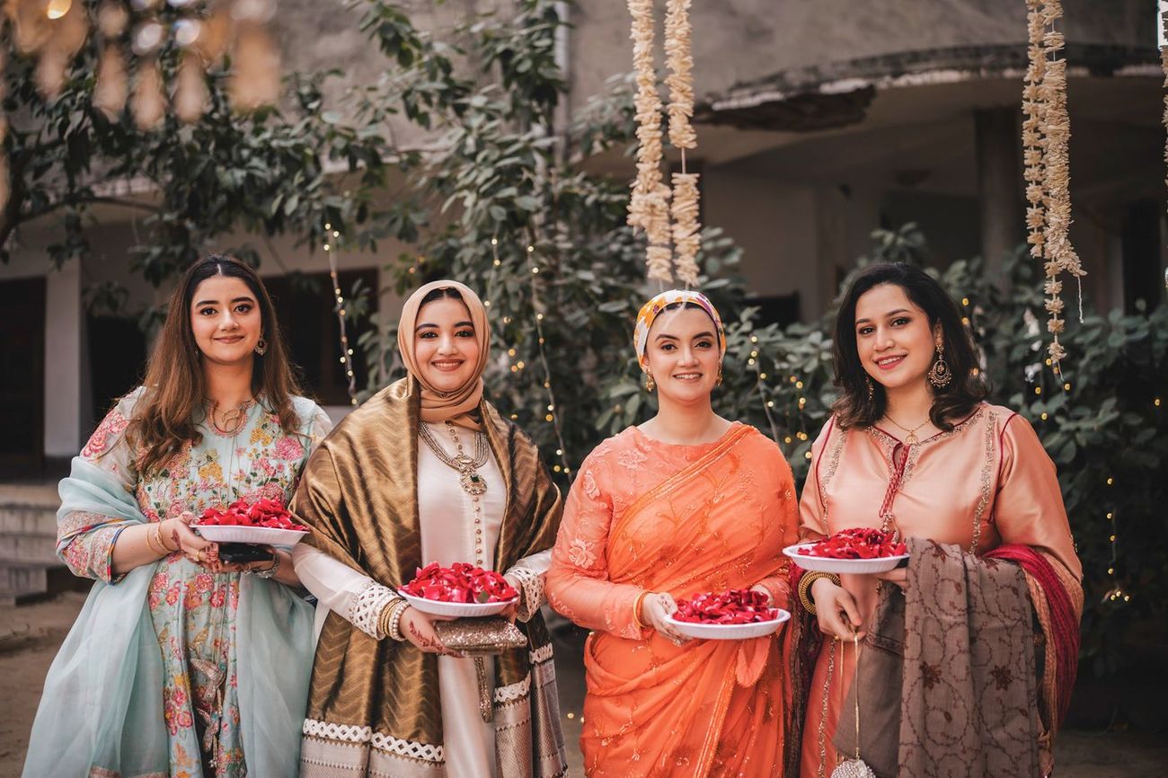 Four women holding plates of red rose petals, posed group photo in the garden venue