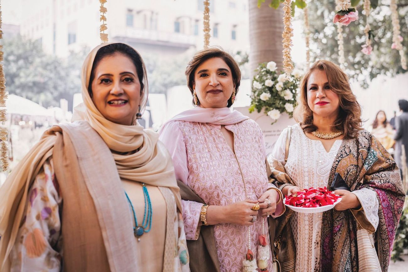 Three older women posed near the welcome sign, one holding a plate of rose petals