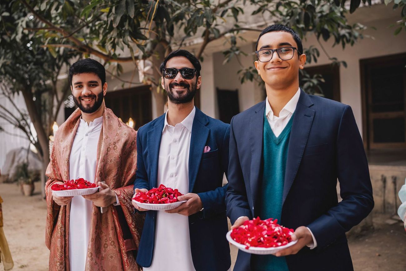 Three young men holding plates of rose petals at the venue