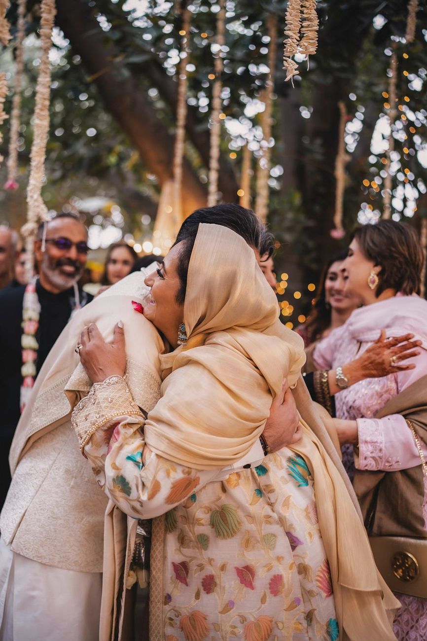Groom embracing an older woman, candid emotional moment under hanging garlands