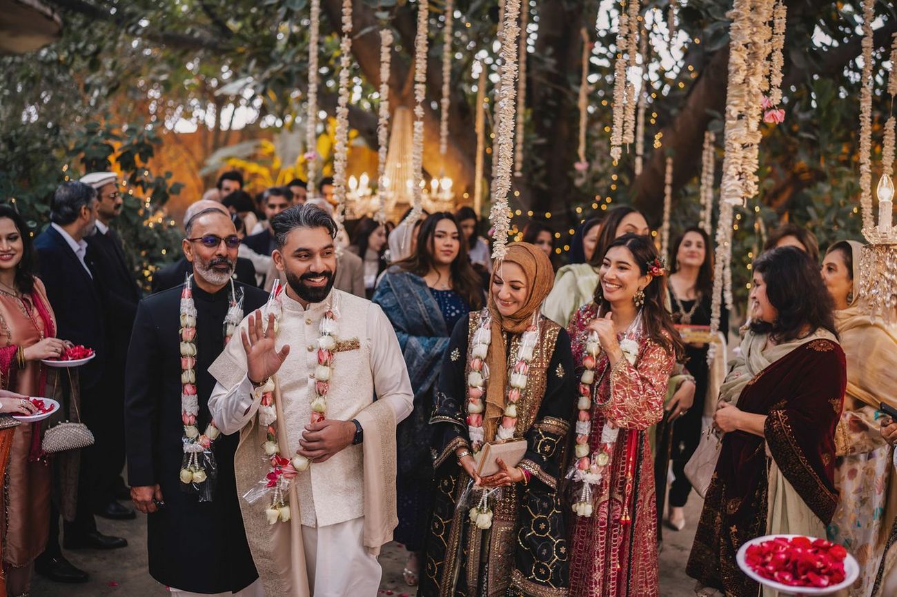 Wide candid shot of the groom walking among guests in floral garlands