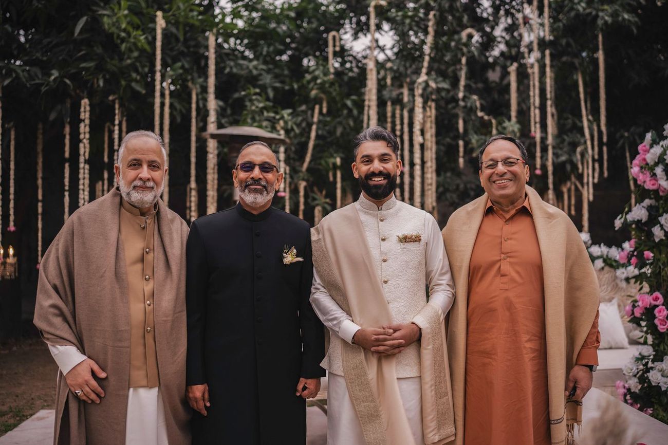 Groom posed with three older male relatives, hanging garlands and florals behind
