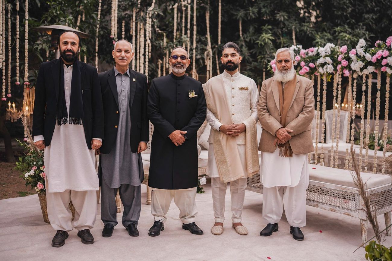 Groom with five male relatives near a white floral-decorated bench