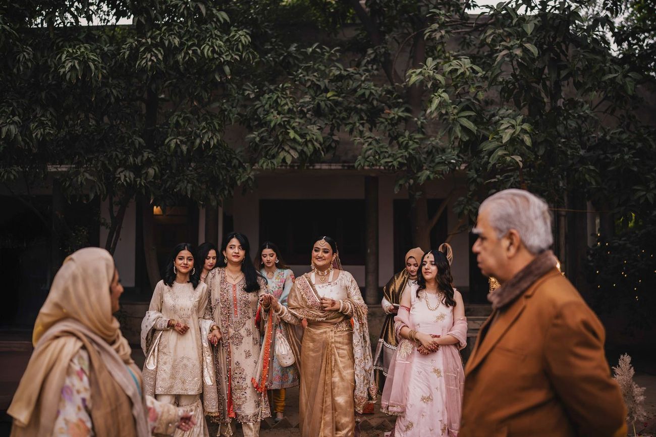 Wide candid shot of the bride walking with bridesmaids under leafy trees