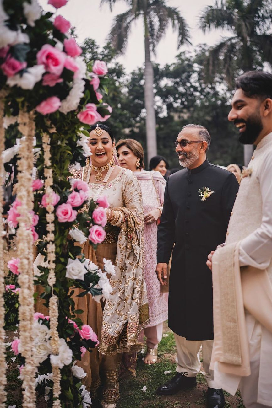 Bride approaching the groom and his father, laughing, palm trees and floral decor visible