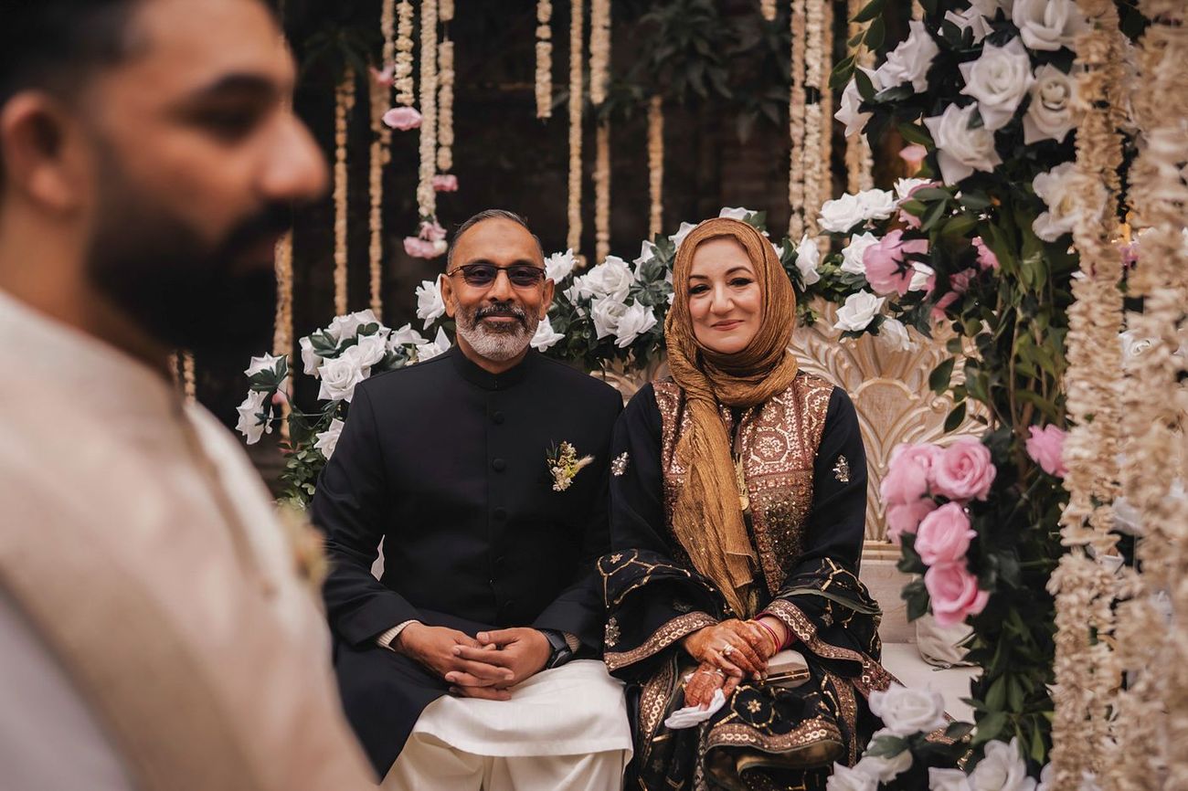 Groom's parents seated on an ornate floral bench, groom blurred in the foreground