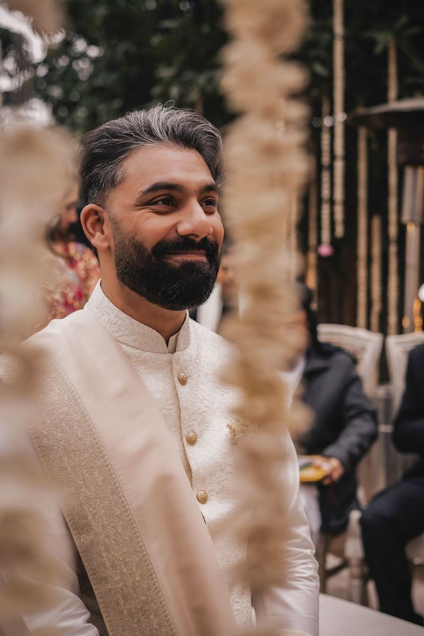 Close-up of the groom smiling, shot through hanging garlands
