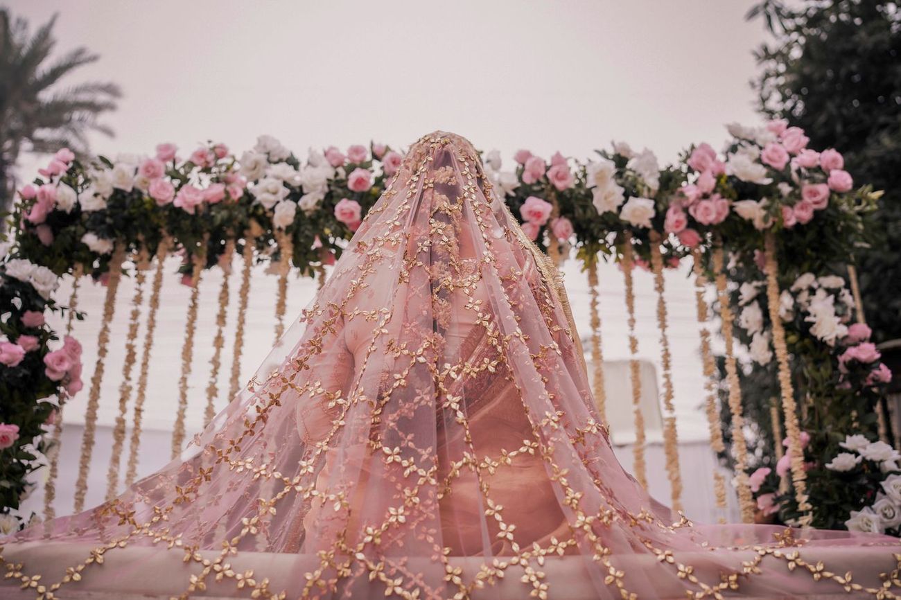 Bride seated with her embroidered dupatta draped fully over her head and face